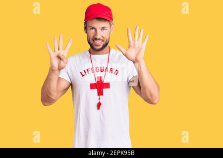 Young caucasian man wearing lifeguard t shirt holding whistle showing and pointing up with fingers number nine while smiling confident and happy. Stock Photo