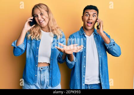 Young interracial couple having conversation talking on the smartphone celebrating achievement with happy smile and winner expression with raised hand Stock Photo