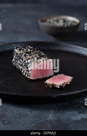Fried tuna steak in black sesame with asparagus on black plate Stock Photo