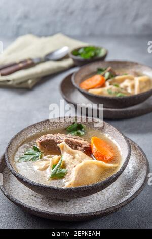 Traditional Jewish food dumplingd kreplach soup in gray bowl. Stock Photo