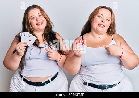 Plus size caucasian sisters woman holding poker chips and cards smiling happy pointing with hand and finger Stock Photo