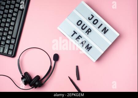 Join our team - text on display lightbox. Flat lay - keyboard, coffee,  black earphones and pen on pink background. Top view. Workplace concept. Stock Photo
