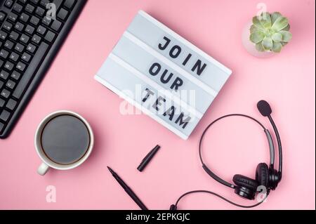 Join our team - text on display lightbox. Flat lay - keyboard, coffee, earphones and pen on pink background. Top view. Workplace concept. Stock Photo