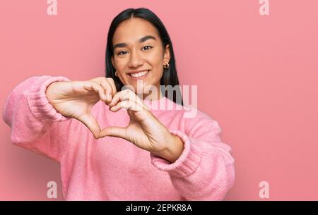 Young asian woman wearing casual winter sweater smiling in love doing heart symbol shape with hands. romantic concept. Stock Photo