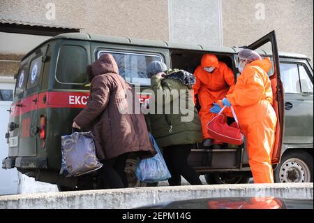 Two medical workers wearing suits to protect against coronavirus help an elderly woman suffering from COVID-19 to leave an ambulance for a hospital in Bohorodchany, western Ukraine. After several delays, Ukraine finally received 500,000 doses of the AstraZeneca vaccine marketed under the name CoviShield, the first shipment of Covid-19 vaccine doses. Ukraine is one of the last in the region to begin vaccination its population. Stock Photo