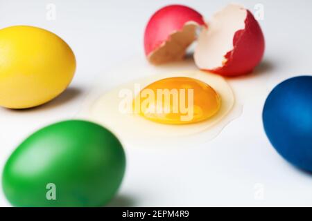 Colorful painted eggs with one cracked, egg white and yolk spilled around, Coronavirus COVID-19 corona virus disease crisis, holiday in home isolation Stock Photo