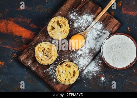 Raw tagliatelle pasta on wooden board with bowl of powder Stock Photo