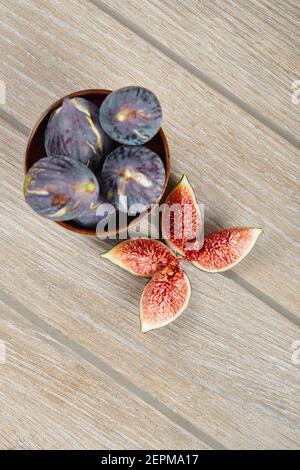 A bowl of black figs and slices of figs on a wooden table Stock Photo