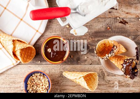 Top view image of a kitchen countertop or table where hand rolled fresh made waffle cones are dipped into melted chocolate and walnut pieces are stick Stock Photo