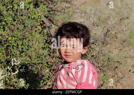 A beautiful little Indian child eating plum fruit in the field , India . concept for India's past smiling child, childhood, children's routine Stock Photo