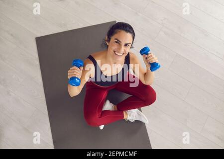 Smiling young fitness slim woman in sportswear sitting on mat and doing abs exercises Stock Photo