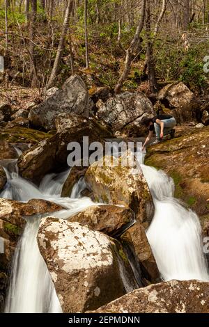 A hiker woman is trying to touch the water on top of a waterfall. A long exposure shoot at a rural location in West Virginia with mountain spring wate Stock Photo