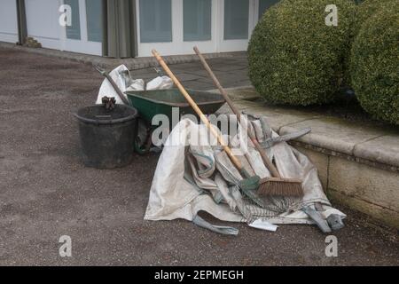 Old Rusty Wheelbarrow with a Brush and Rake on a Footpath in a Garden in Rural Devon, England, UK