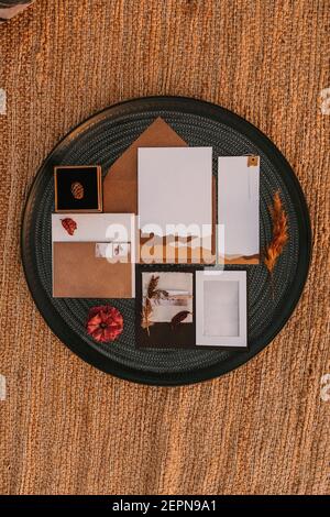 Top view of white greeting cards placed on black round tray with bright plants on wicker surface during wedding celebration Stock Photo