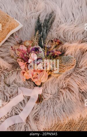 From above arrangement of fresh pink flowers with plant and decorative branch placed on soft plaid with ribbon during wedding celebration Stock Photo
