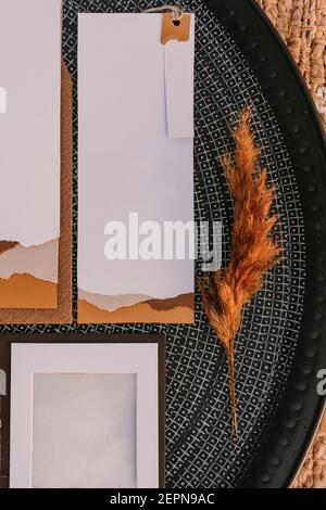 Top view of white greeting cards placed on black round tray with bright plants on wicker surface during wedding celebration Stock Photo