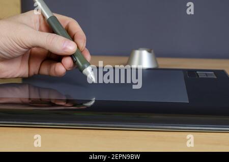 A designer's hand drawing with a special pen on the screen of a graphics tablet. A man's hand and a professional device for designers in close-up.  Si Stock Photo