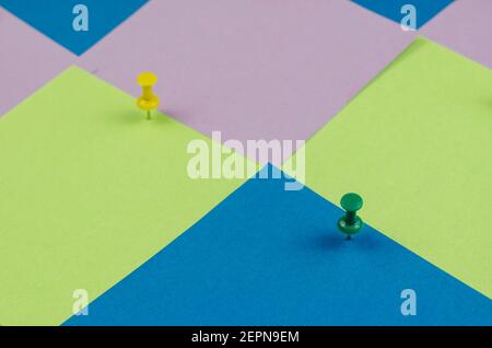 Two pushpins and many colorful sticky notes. Green and yellow pushpins on a multicolored background. Side view at an angle. Selective focus. Stock Photo