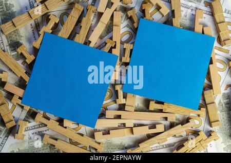 Two blue squares on top of a wooden puzzle and money. Blank paper stickers for notes and One hundred American dollar bills in the background. Finance, Stock Photo