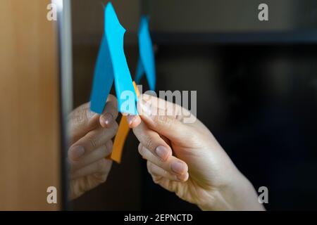 Crop anonymous executive taking notes on bright paper stickers on glass wall in office Stock Photo