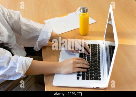 crop female entrepreneur browsing netbook while sitting with paper document and eco friendly glass bottle of fresh juice Stock Photo