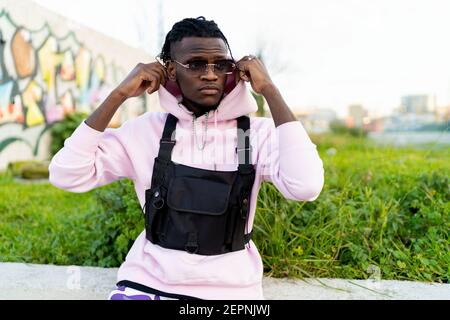 Confident African American male putting on hood sitting in stylish sunglasses and looking away Stock Photo