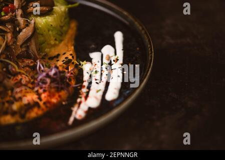 Close up crop view of yummy vegan dish with zucchini spaghetti and sauteed mushroom slices covered with red berries and alfalfa sprouts on dark backgr Stock Photo