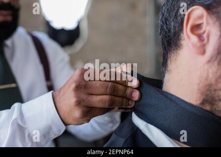 Cropped unrecognizable ethnic male beauty master putting on cape protection on client in hairdressing salon Stock Photo