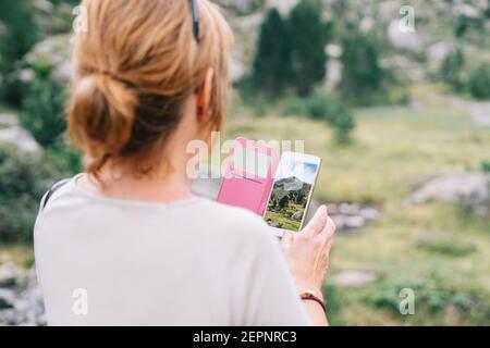 Back view anonymous female taking pictures on smartphone of amazing stony verdant highlands in Ruda Valley in Catalan Pyrenees Stock Photo