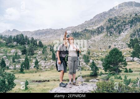 Mature trekkers in casual apparel taking self portrait on cellphone against green mount under cloudy sky Stock Photo