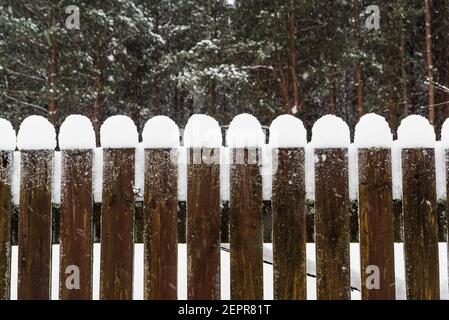 Smooth snow caps on the wooden planks of the yard fence. Stock Photo