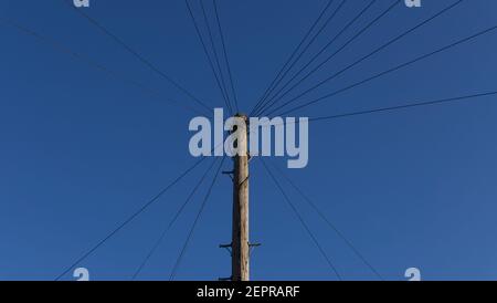 Wooden telegraph pole with wires leading off at angles against blue sky Stock Photo