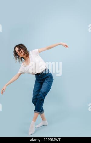 Artistic contemporary dancer poses in front of blue studio background. She's walking on the line, crossing her legs slightly, bending forward. Arms sp Stock Photo