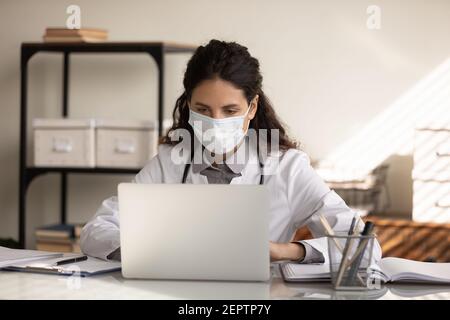 Close up confident female doctor wearing face mask using laptop Stock Photo