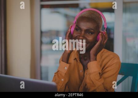 black adult woman listens to music looks happy while working on her computer in a coffee shop focus on the face Stock Photo