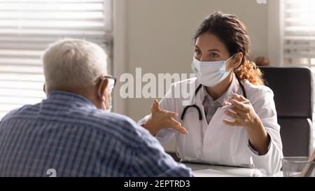 Close up female therapist wearing face mask consulting mature patient Stock Photo