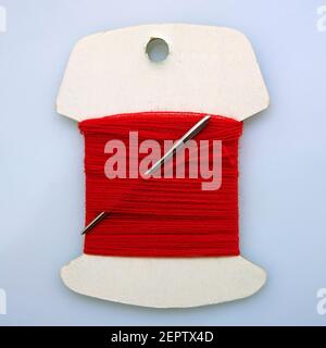 Close-up of a red thread spool with a needle threaded through it on a simple background Stock Photo