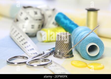 sewing accessories with blue and yellow threads, tape measure and scissors on fabric background Stock Photo