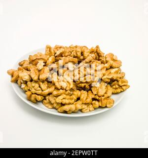 A large serving of golden-brown walnut halves on a white plate against a plain background Stock Photo
