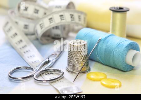 sewing tools with scissors, threads, needle and tape measure. Dressmakers accessories on blue and yellow fabrics Stock Photo