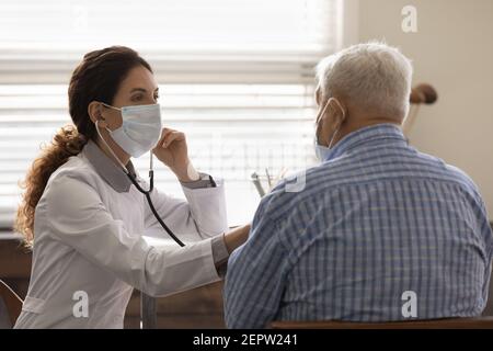 Female doctor wearing face mask checking mature man lungs Stock Photo