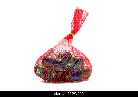A colorful collection of marbles in a red mesh bag on a white background showcasing various designs and patterns Stock Photo
