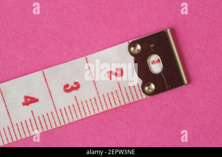 Close up of white measuring tape isolated on pink background showing red numbers from one to four Stock Photo
