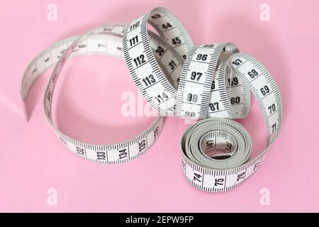 Unrolled spiral dressmaker's tape measure isolated on pink background Stock Photo
