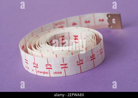 Measuring tape isolated on purple background and rolled up on itself Stock Photo