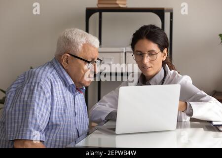 Close up female professional doctor consulting mature patient, using laptop Stock Photo