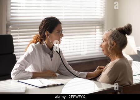 Side view female doctor using stethoscope, checking mature patient lungs Stock Photo