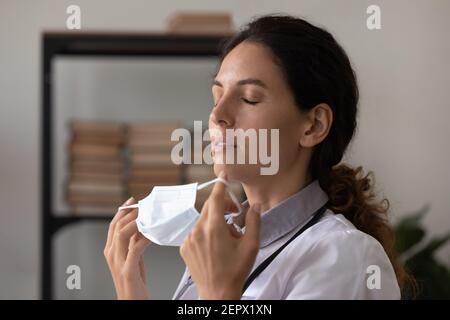 Close up exhausted woman doctor taking off medical face mask Stock Photo