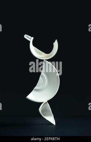 Broken cup balancing construction, porcelain shards on a black background Stock Photo