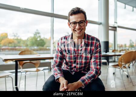 Portrait of a cheerful young businessman sitting in office. Happy young professional smiling at camera. Stock Photo